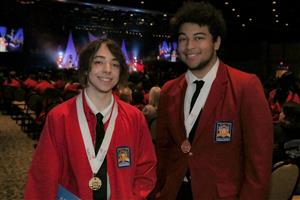 Owen and Cullen in front of stage in red jackets with gold medals